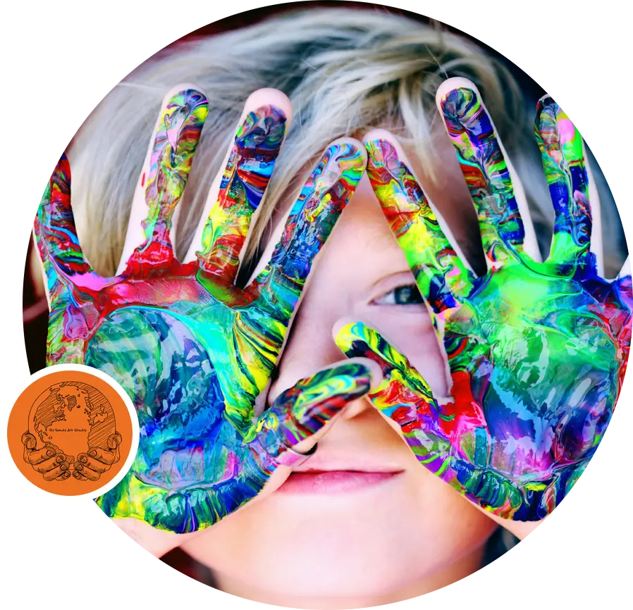 A child with colorful paint on their hands holds them up in front of their face, creating a vivid display of mixed colors—an inspiring moment of healing through art.